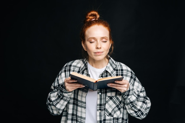 Portrait, de, heureux, jeune femme, étudiant collège, à, yeux fermés, tenue, livres, sur, isolé, fond noir