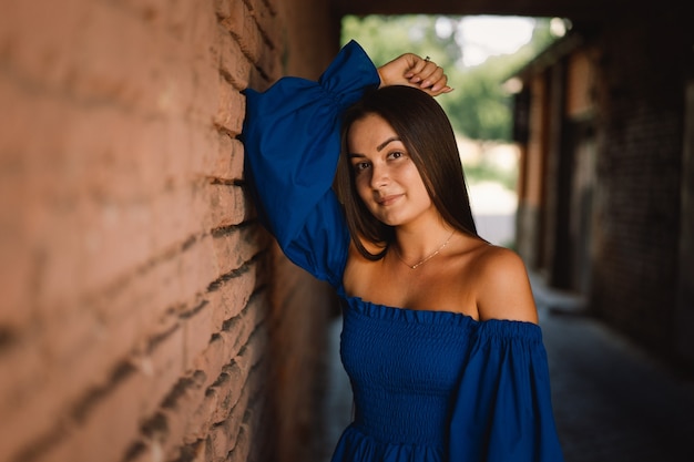 Portrait heureux jeune femme vêtue d'une robe bleue en riant en regardant la caméra debout sur la rue urbaine ba...