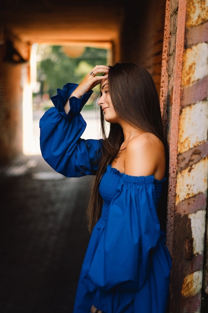 Portrait heureux jeune femme vêtue d'une robe bleue en riant en regardant la caméra debout sur la rue urbaine ba...