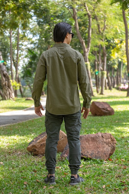 Portrait de l'heureux jeune homme asiatique en chemise à manches longues et pantalon vert debout dans le parc