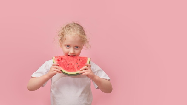 Portrait heureux jeune petite fille tient une tranche de pastèque sur fond rose coloré