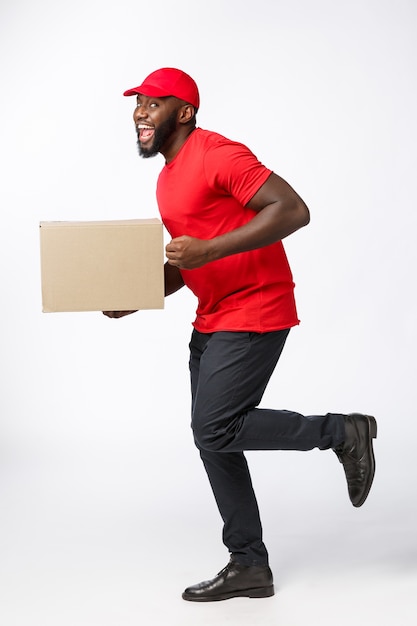 Portrait de l'heureux livreur afro-américain en tissu rouge à pied pour envoyer un colis au client.