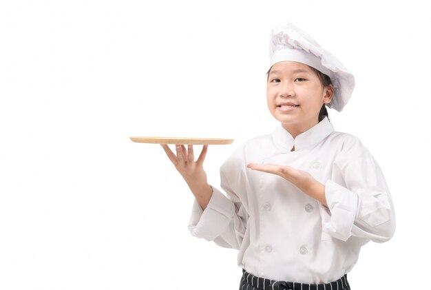 Portrait Heureux petit chef en uniforme présentant un plat et souriant, assiette vide prête pour la nourriture isolée sur un mur blanc et copiez l'espace.