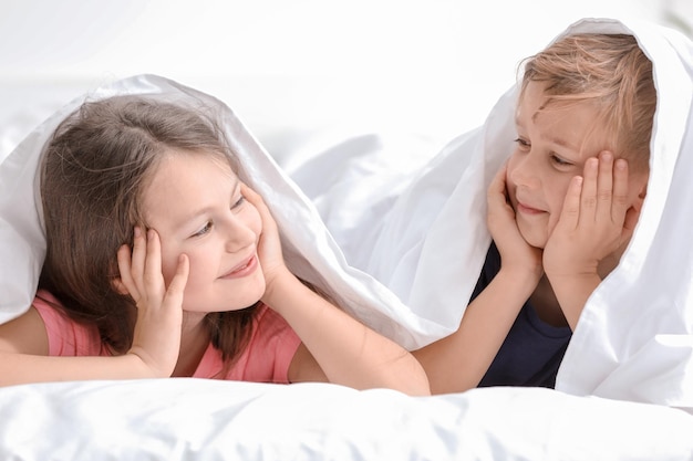 Portrait d'heureux petit frère et soeur allongés sur le lit sous une couverture