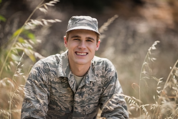 Portrait de l'heureux soldat militaire accroupi dans l'herbe dans le camp d'entraînement