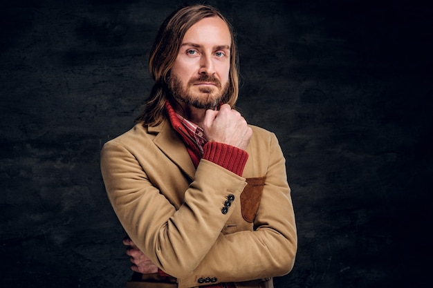 Portrait d'un hipster barbu pensif en veste et pull rouge sur fond sombre.