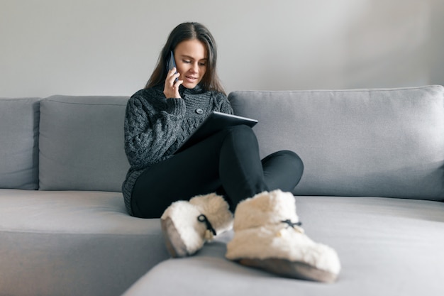 Portrait d&#39;hiver automne de la jeune fille en pull chaud, à la maison sur le canapé avec tablette numérique et téléphone.