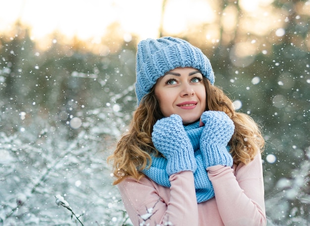 Portrait d'hiver de la belle jeune femme brune bouclée portant une écharpe tricotée bleue couverte de neige.