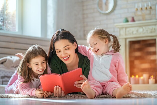 Portrait d'hiver d'une famille aimante heureuse Jolie jeune mère lisant un livre à ses filles à la maison