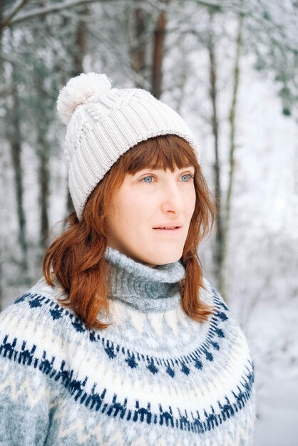 Portrait d'hiver d'une femme dans un chapeau chaud et un pull sur fond de forêt enneigée