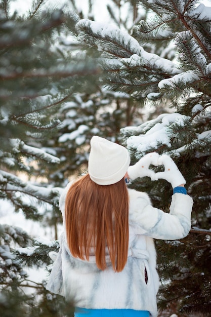 Portrait d'hiver d'une fille dans la forêt jouant avec de la neige dans un chapeau blanc chaud Année du lapin