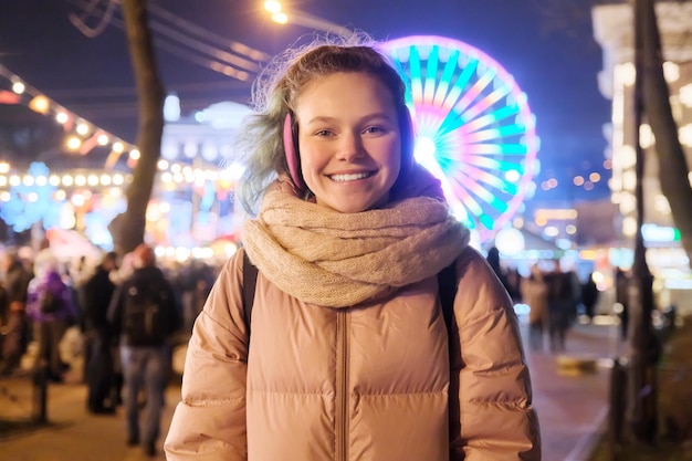 Portrait d'hiver d'une jeune adolescente heureuse au marché de Noël. Lumières, guirlandes lumineuses, fond de grande roue