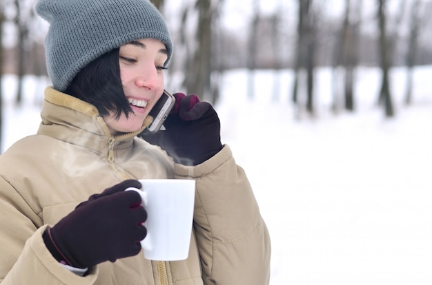 Portrait d&#39;hiver de jeune fille avec une tasse de café et smartphone