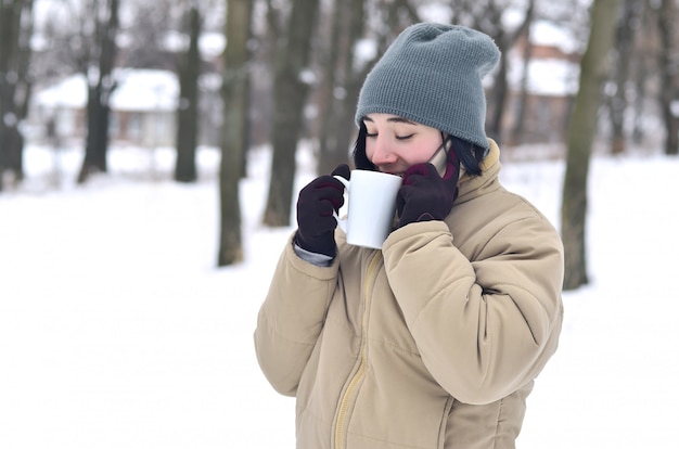 Portrait d&#39;hiver de jeune fille avec une tasse de café et smartphone