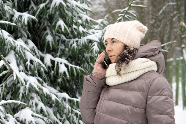 Photo portrait d'hiver en plein air. belle femme de 45 ans parlant sur un téléphone portable dans un parc d'hiver enneigé.