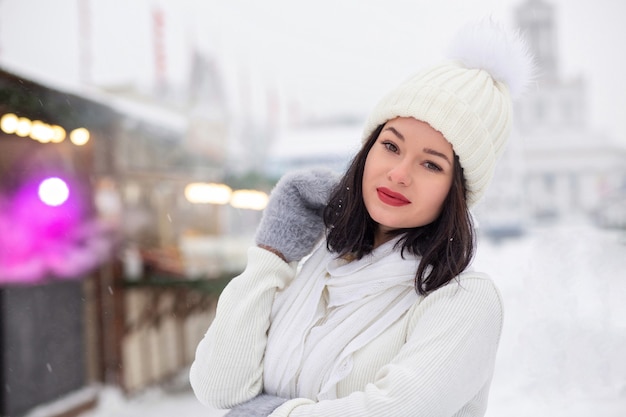 Le portrait d'hiver de rue d'une jeune femme à la mode porte un bonnet et une écharpe tricotés posant dans des chutes de neige. Espace libre