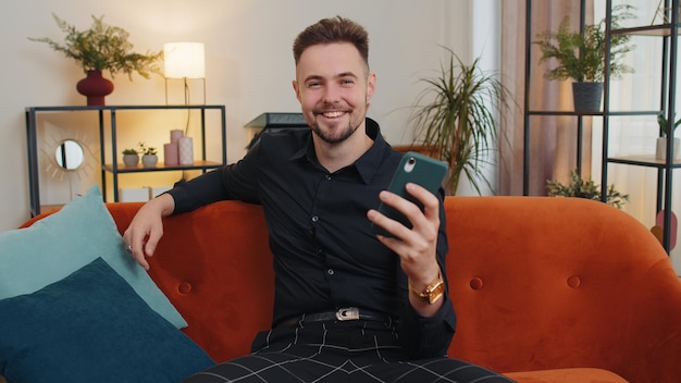 Portrait d'un homme adulte assis sur un canapé en utilisant un smartphone partage des messages sur l'application de médias sociaux