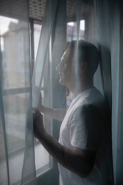 Photo portrait d'un homme adulte avec rideaux et ombre depuis la fenêtre