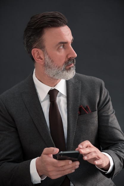 Portrait d'homme d'affaires adulte portant un costume à la mode et assis dans un studio moderne sur une chaise élégante sur fond noir. Maquette horizontale. Photo de haute qualité