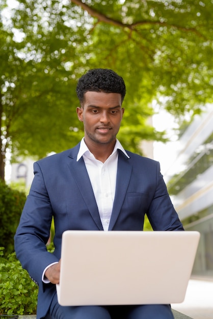 Portrait d'homme d'affaires africain utilisant un ordinateur portable à l'extérieur, tir vertical