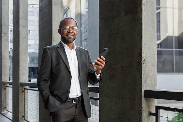 Portrait d'un homme d'affaires afro-américain mature à l'extérieur d'un immeuble de bureaux tenant un téléphone dans