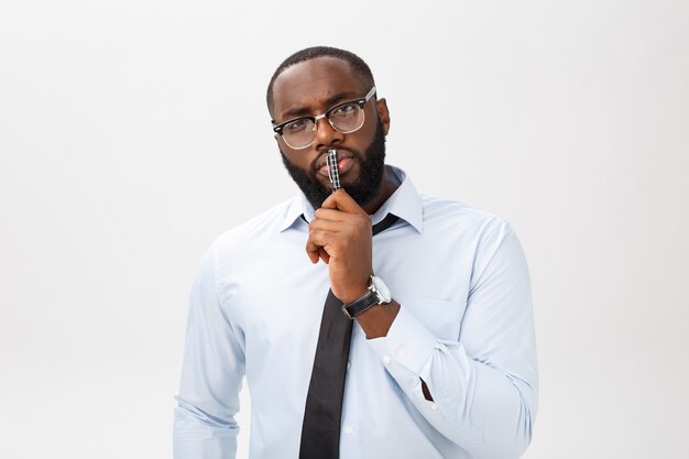 Portrait d'un homme d'affaires afro-américain pensif dans un costume gris pensant avec un stylo sur sa bouche