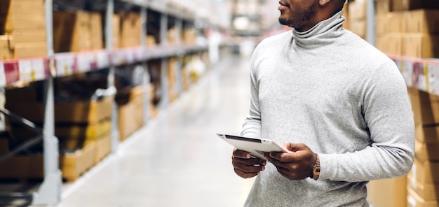 Photo portrait d'un homme d'affaires afro-américain souriant détails de la commande sur tablette vérifiant les marchandises et les fournitures sur les étagères avec un fond de marchandises dans l'exportation logistique et commerciale de l'entrepôt