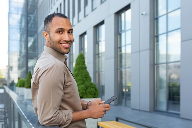 Portrait d'un homme d'affaires afro-américain tenant un téléphone souriant et regardant le bureau de la caméra