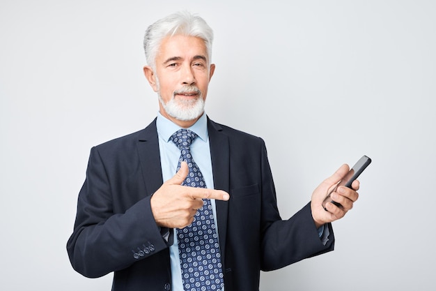 Photo portrait d'un homme d'affaires âgé en costume montrant un écran de téléphone portable vide avec un visage excité personne avec un smartphone isolé sur un fond blanc