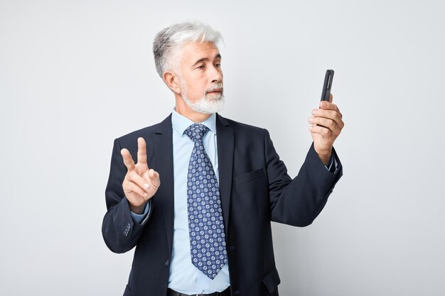 Photo portrait d'un homme d'affaires âgé en costume prenant une photo selfie sur un téléphone portable blogueur avec un smartphone isolé sur un fond blanc