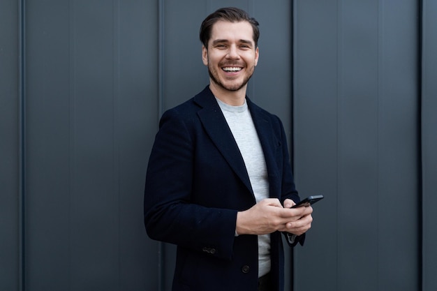 Portrait d'un homme d'affaires d'âge moyen fort utilisant un téléphone portable et un large sourire contre un gris