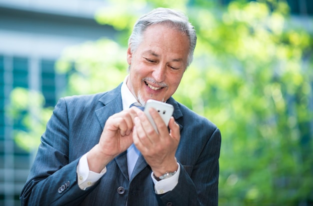 Portrait d'un homme d'affaires âgé souriant utilisant son smartphone mobile à l'extérieur