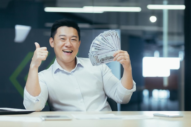 Portrait d'un homme d'affaires asiatique heureux au bureau avec de l'argent en espèces homme souriant et regardant