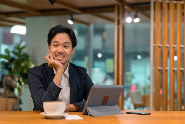 Portrait d'un homme d'affaires asiatique heureux dans un café à l'aide d'une tablette numérique