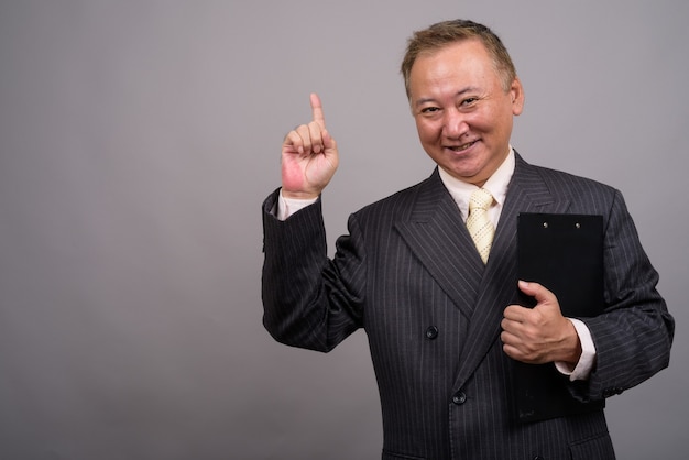 Portrait d'homme d'affaires asiatique mature contre mur gris