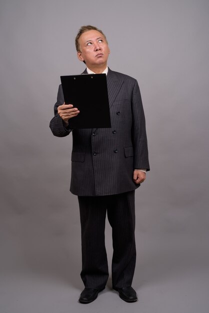 Portrait d'homme d'affaires asiatique mature contre mur gris