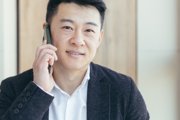 portrait d'homme d'affaires asiatique réussi et souriant souriant parlant au téléphone dans un costume d'affaires