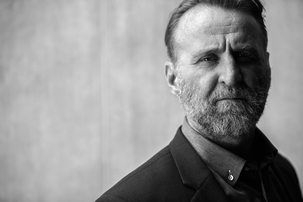 Portrait d'homme d'affaires barbu beau mature aux cheveux blonds en costume contre un mur de béton à l'extérieur en noir et blanc