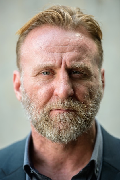 Portrait d'homme d'affaires barbu beau mature en costume contre un mur de béton à l'extérieur