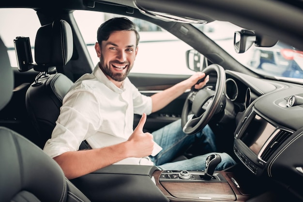 Portrait d'un homme d'affaires caucasien heureux assis dans la nouvelle voiture montrant les pouces vers le haut et regardant la caméra