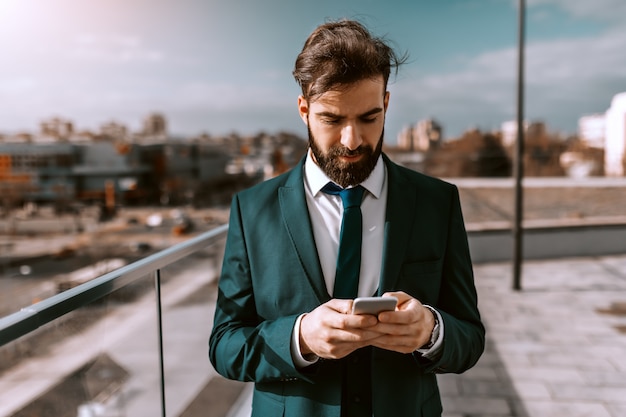 Portrait d'homme d'affaires caucasien prospère en tenue de soirée à l'aide d'un téléphone intelligent sur le toit.