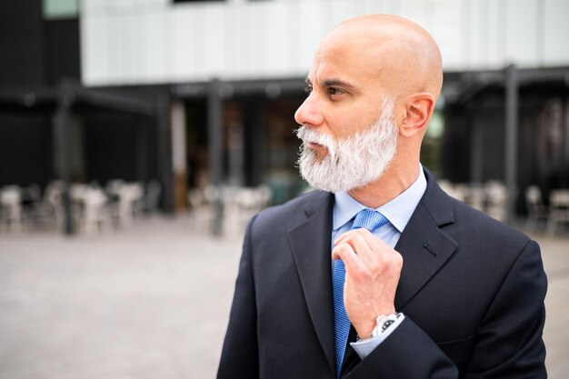 Portrait d'un homme d'affaires chauve et élégant avec une barbe blanche à l'extérieur ajustant sa cravate