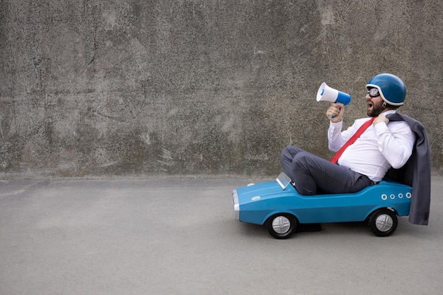 Portrait d'homme d'affaires drôle en plein air Homme conduisant une voiture à pédales rétro et criant par haut-parleur Retour au démarrage du travail et concept d'idée d'entreprise