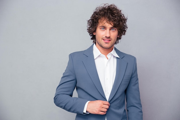 Portrait d'un homme d'affaires heureux avec des cheveux bouclés à l'avant sur un mur gris