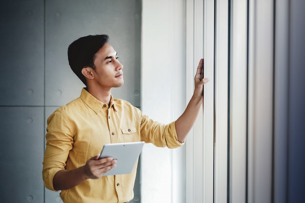 Portrait d&#39;homme d&#39;affaires heureux, debout près de la fenêtre du bureau. À l&#39;aide d&#39;une tablette numérique