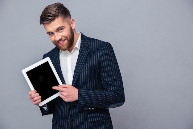 Portrait d'un homme d'affaires heureux montrant l'écran de l'ordinateur tablette sur mur gris