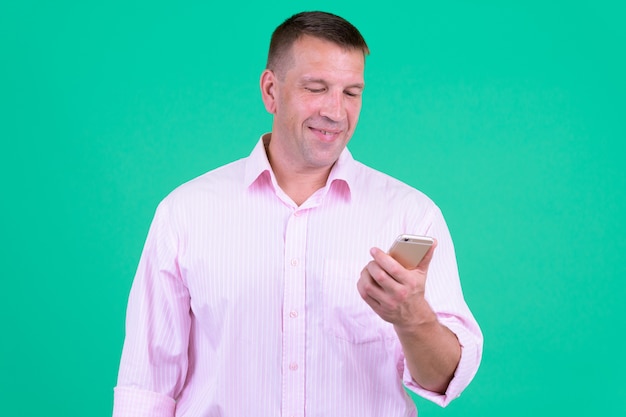 Portrait d'homme d'affaires macho mature portant une chemise rose contre un mur de couleur