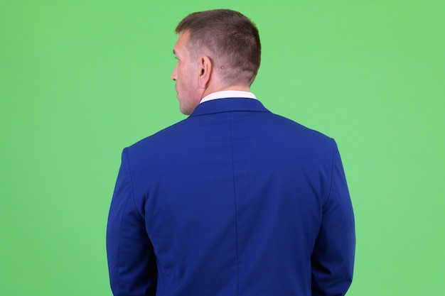 Portrait d'homme d'affaires macho mature portant un costume bleu contre la clé chroma avec mur vert