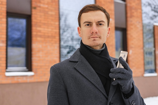 Portrait d'homme d'affaires en manteau avec téléphone portable regardant la caméra contre l'immeuble de bureaux