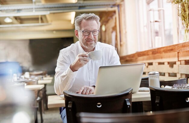 Portrait d'un homme d'affaires mature confiant dans un café utilisant un ordinateur portable